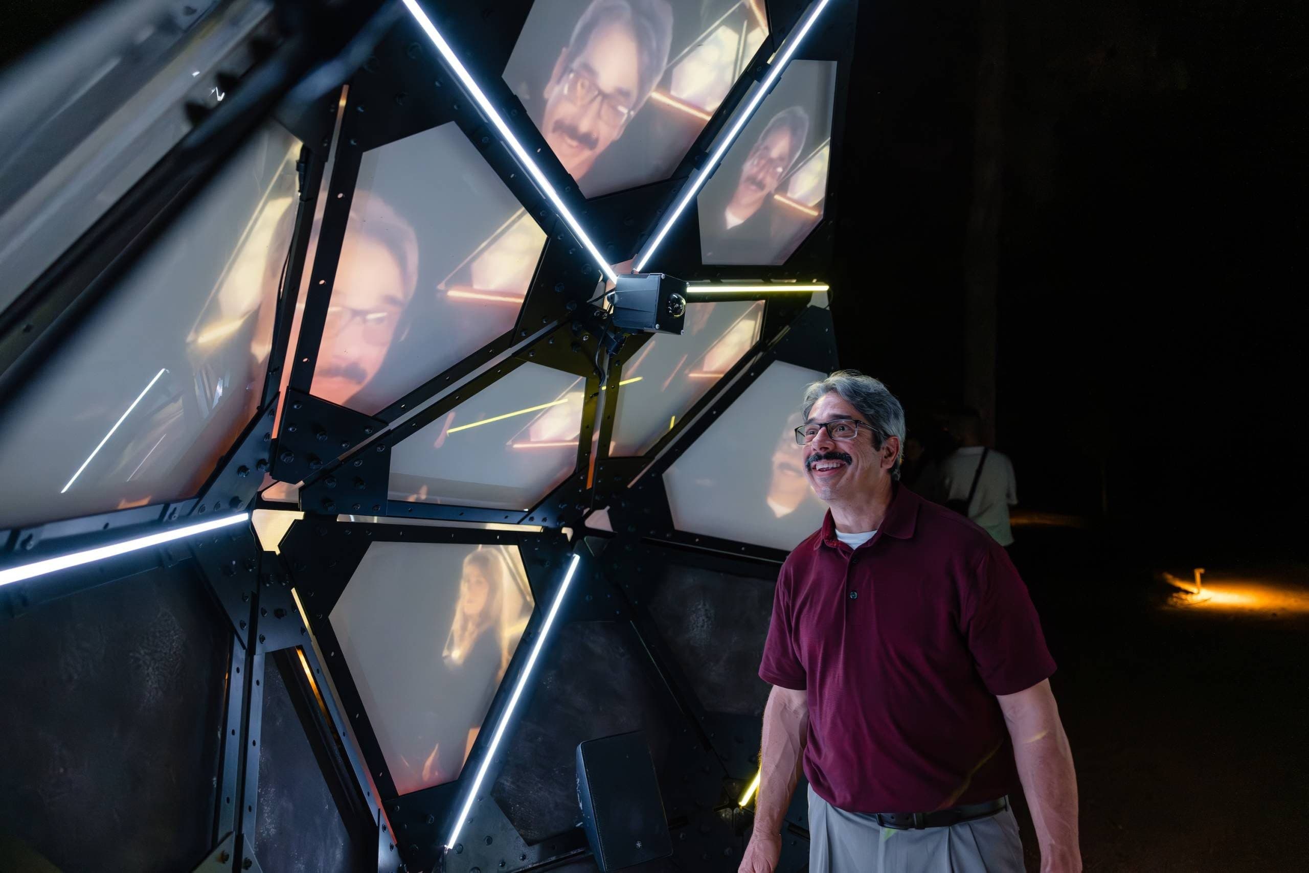 A man grins and looks at the video screens of the interactive installation Broken Time Machine by Klip Collective