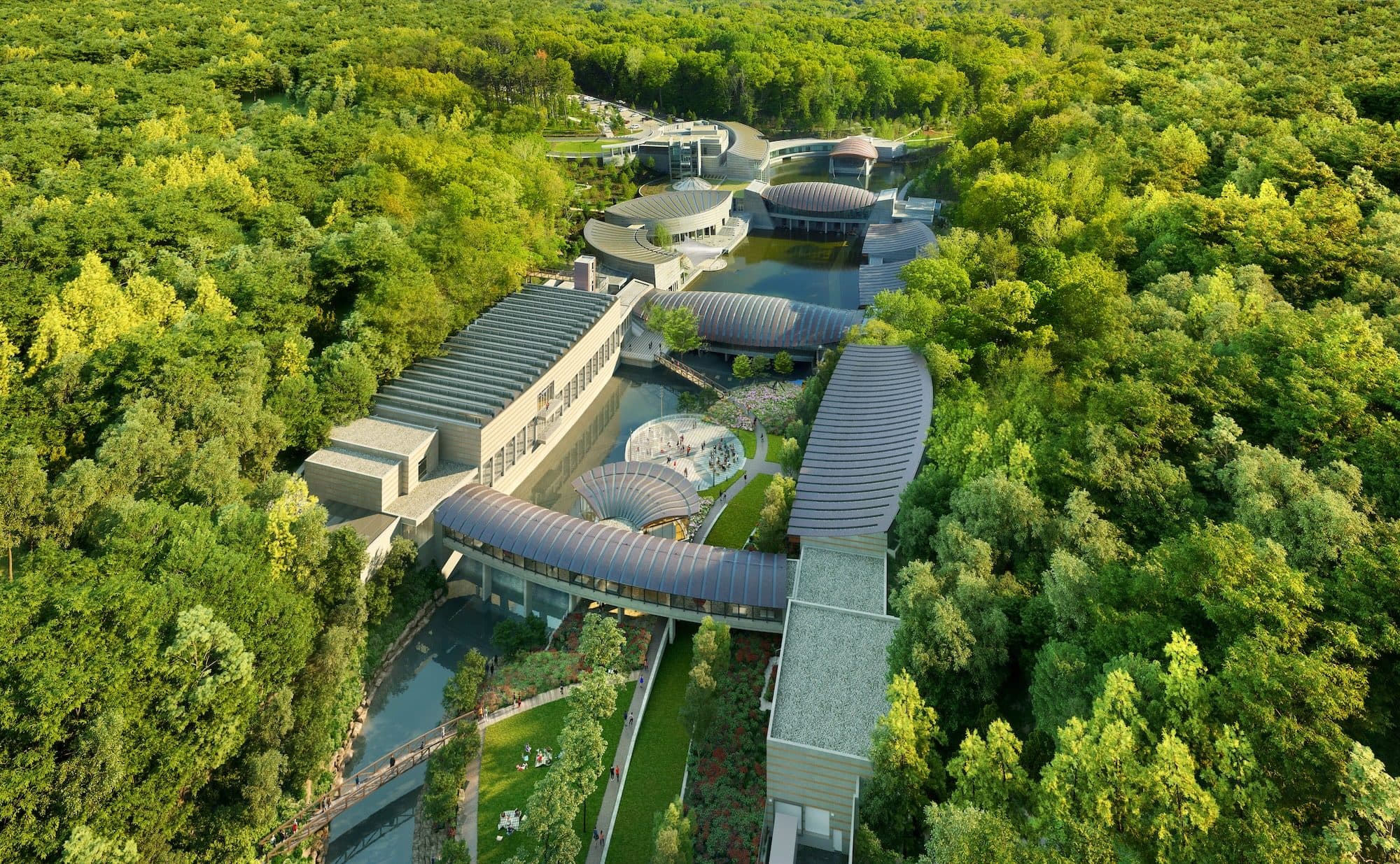 Modern architectural complex with curved roofs in forest, arranged around a pond with pathways.